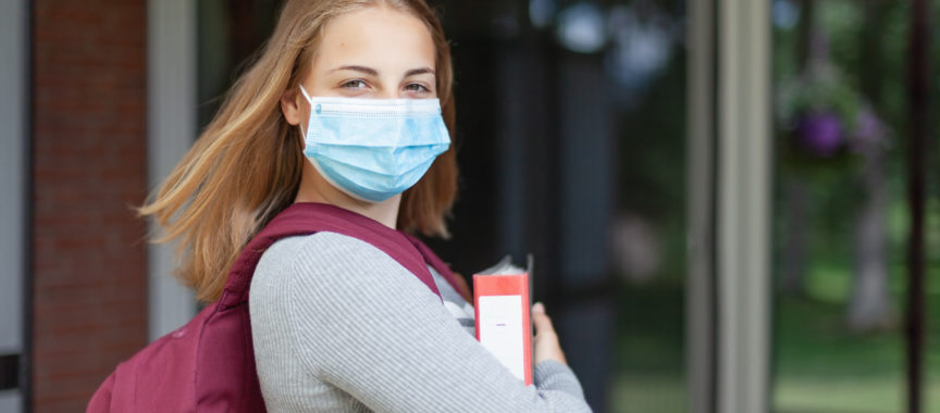 Mädchen mit Maske und Ordner vor Schule