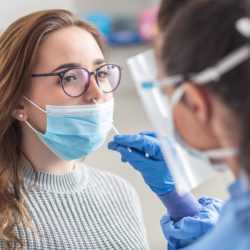 Female patient wearing mask over mouth is having sample taken from nose for a pcr test for Covid 19.