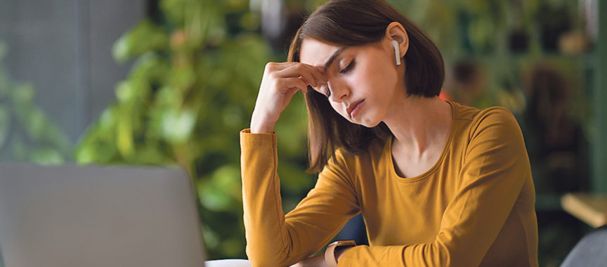 Exhausted young woman using earpods and laptop at cafe